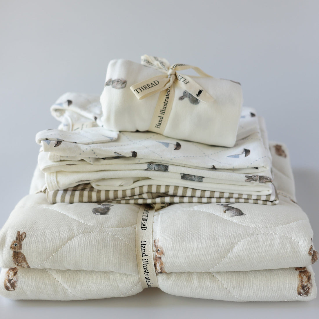 Stack of newborn baby essentials including bodysuit, babygrows, baby blankets, and swaddle wraps – must-haves for new parents