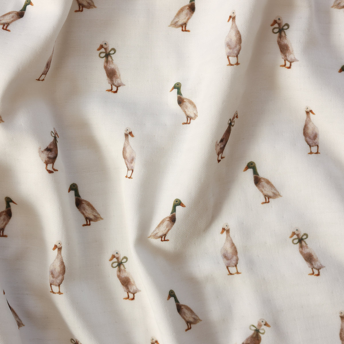 A close-up of a fabric surface with a repeating print of mallards in muted brown, gray, green, and orange tones on an off-white background.