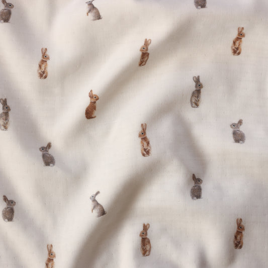 A close-up of a cream-colored fabric with a repeating pattern of small rabbits in brown, tan, and gray tones.