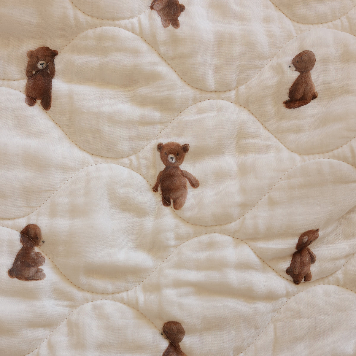 Close-up of a quilted cream fabric with a repeating pattern of small brown teddy bears.