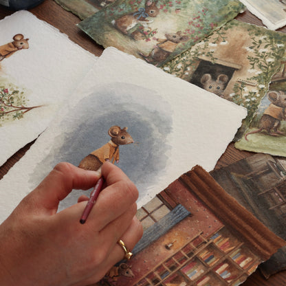 Hand holding a pen over a piece of paper with a mouse illustration, surrounded by other illustrated mouse artworks.