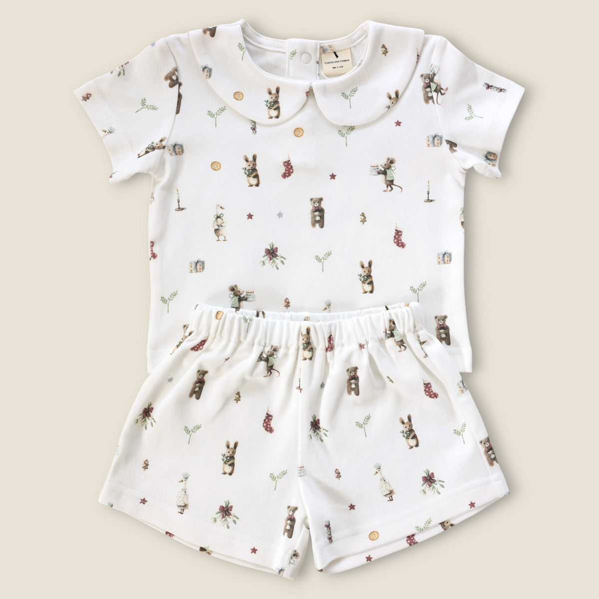 A baby two-piece outfit set consisting of a short-sleeve top and matching shorts in white, decorated with a whimsical print of bears, rabbits, flowers, and stars. The top features a Peter Pan collar, and both pieces are laid flat on a light beige background.