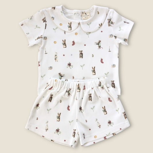 A baby two-piece outfit set consisting of a short-sleeve top and matching shorts in white, decorated with a whimsical print of bears, rabbits, flowers, and stars. The top features a Peter Pan collar, and both pieces are laid flat on a light beige background.