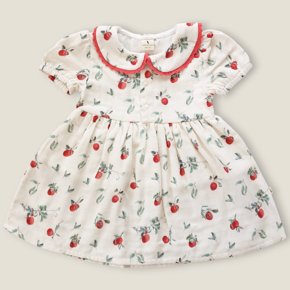 A baby girl's short-sleeve dress with a white base, featuring a red and green cherry print, a red ruffled Peter Pan collar, and a gathered waist.
