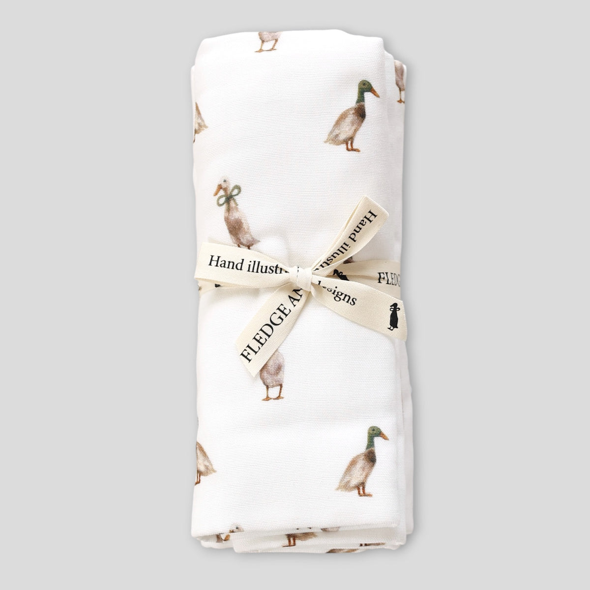 A folded white muslin cloth featuring a printed pattern of mallards, tied with a cream ribbon printed with the brand name 'FLEEDGE designs', set against a solid gray background.