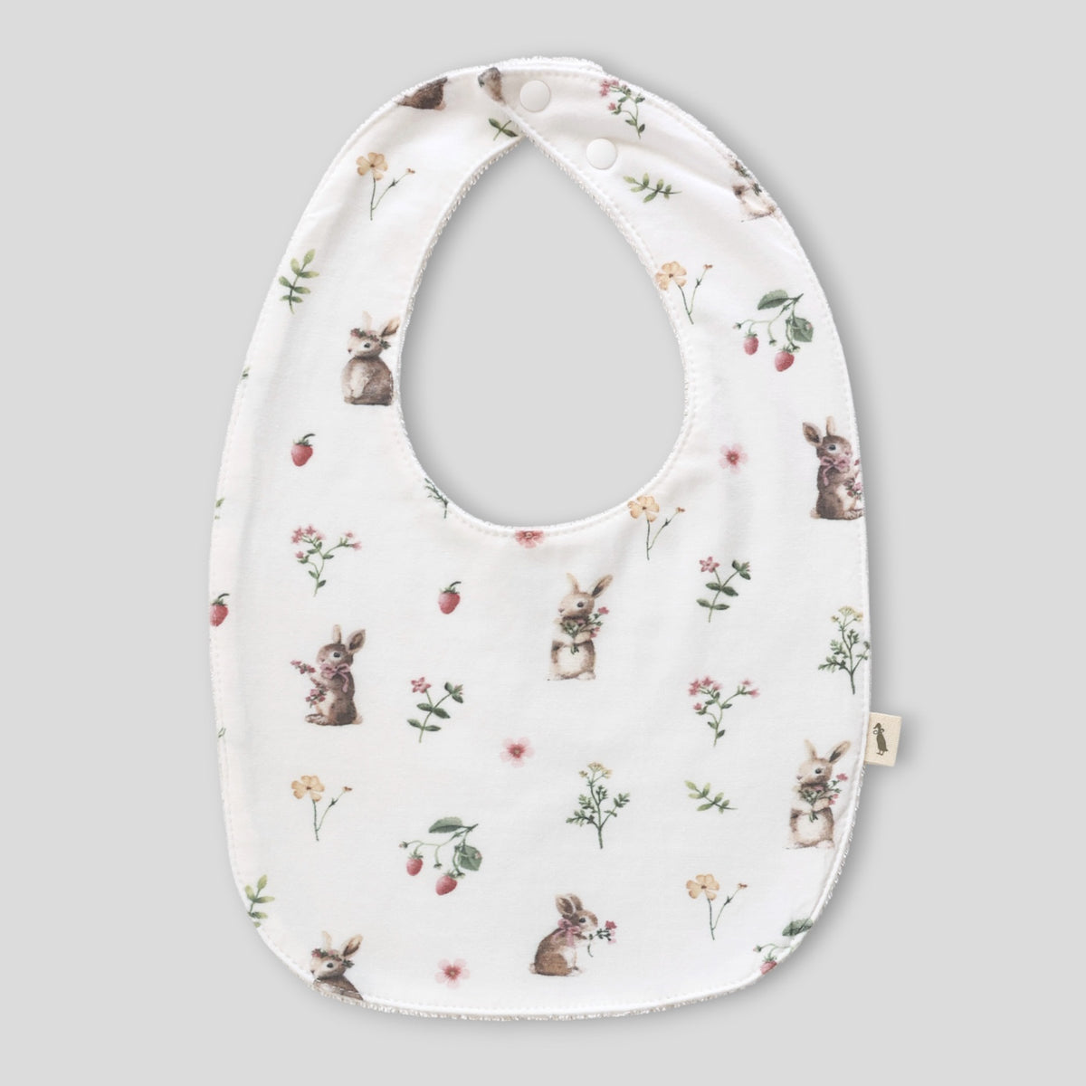 A white baby bib with an all-over print of rabbits, strawberries, and small wildflowers, shown against a solid gray background.