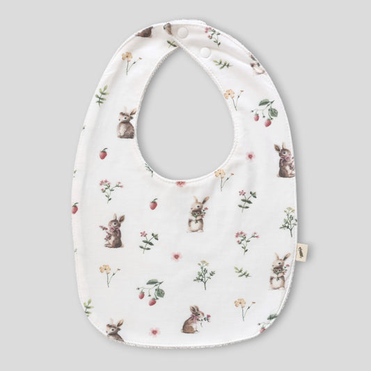A white baby bib with an all-over print of rabbits, strawberries, and small wildflowers, shown against a solid gray background.