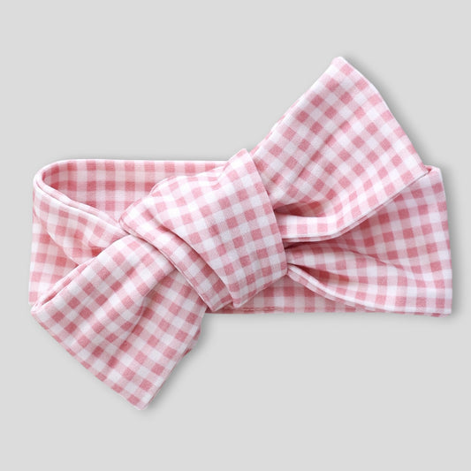 A pink and white gingham bow headband, styled with a large central knot, shown against a solid light gray background.