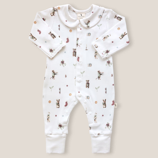 A white long-sleeve baby romper with a button-down front, featuring an all-over print of woodland animals, flowers, and small icons. The romper has a Peter Pan collar and is photographed flat against a solid light beige background.