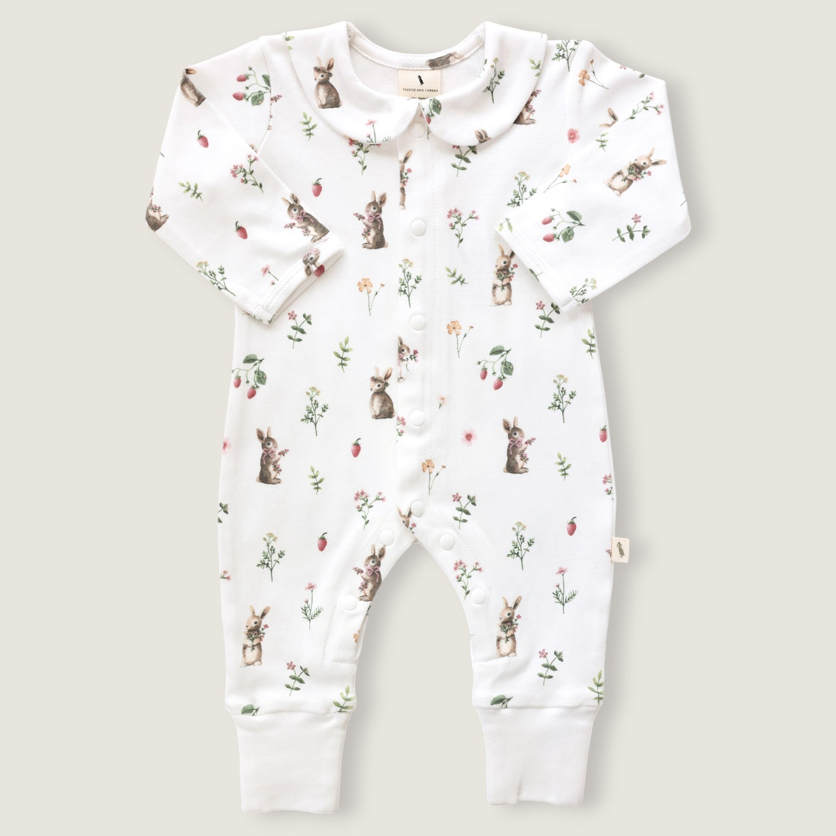 A baby long-sleeve footless romper in white, featuring an all-over print of rabbits, strawberries, and small wildflowers. The romper has a Peter Pan collar, snap-button front, and ribbed cuffs at the ankles, shown flat on a light beige background.