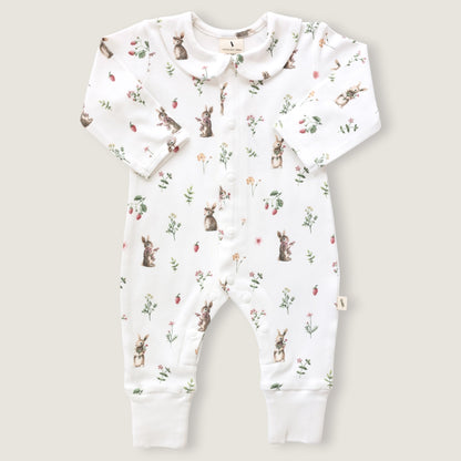 A baby long-sleeve footless romper in white, featuring an all-over print of rabbits, strawberries, and small wildflowers. The romper has a Peter Pan collar, snap-button front, and ribbed cuffs at the ankles, shown flat on a light beige background.