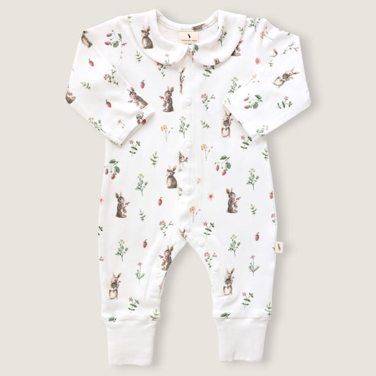 A baby long-sleeve footless romper in white, featuring an all-over print of rabbits, strawberries, and small wildflowers. The romper has a Peter Pan collar, snap-button front, and ribbed cuffs at the ankles, shown flat on a light beige background.