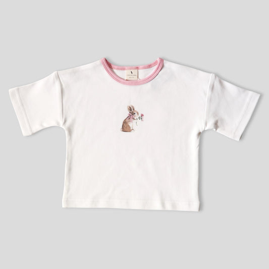 A white short-sleeve baby t-shirt with a pink ribbed crew neck and a small watercolor bunny graphic on the chest, displayed flat on a light gray background.
