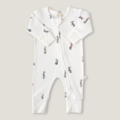 A white long-sleeve baby footless one-piece sleeper with a front zipper and an all-over watercolor rabbit print, shown flat on a light beige background.