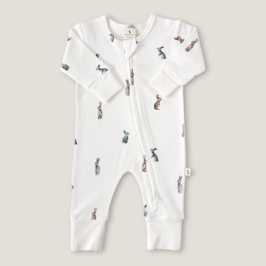 A white long-sleeve baby footless one-piece sleeper with a front zipper and an all-over watercolor rabbit print, shown flat on a light beige background.