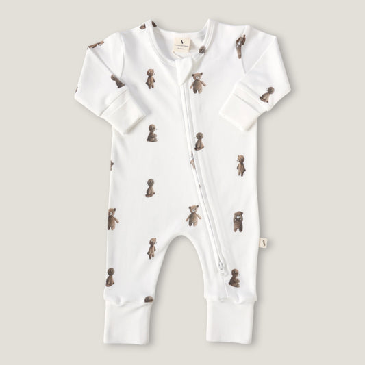 A white long-sleeve baby footless one-piece sleeper with a front zipper and an all-over print of small brown teddy bears, shown flat on a light beige background.